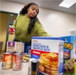 A young woman organizes a box of dry goods received by Replenish.